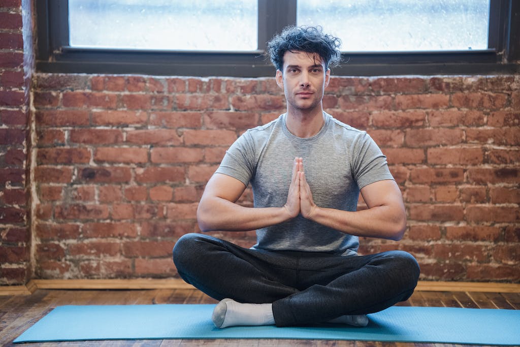 Photo by Klaus Nielsen Full body of focused male sitting in Sukhasana with praying hands while practicing yoga on sports mat